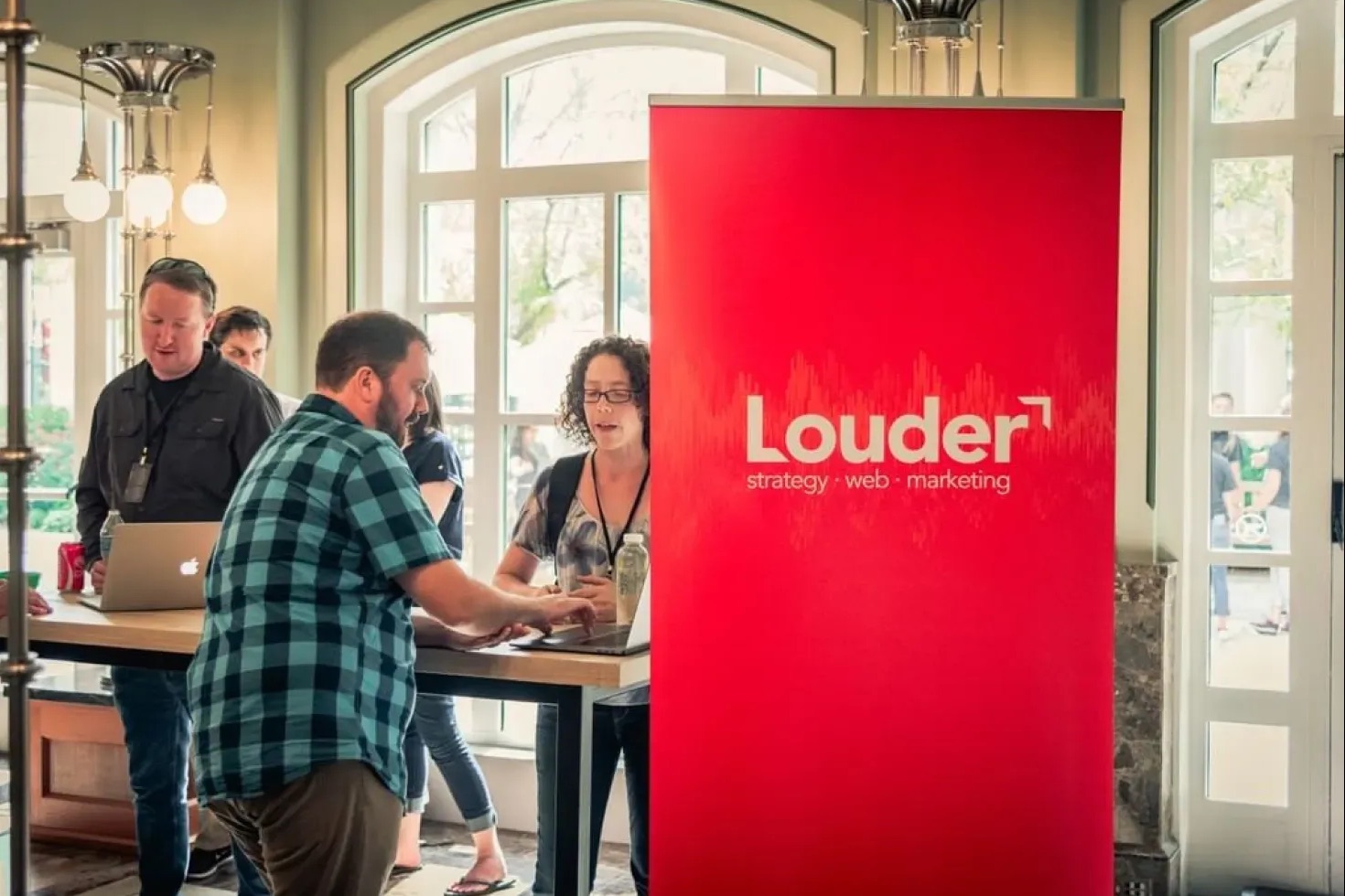 The Louder team reviewing a nonprofit's website with them at a conference booth, beside a red Louder banner