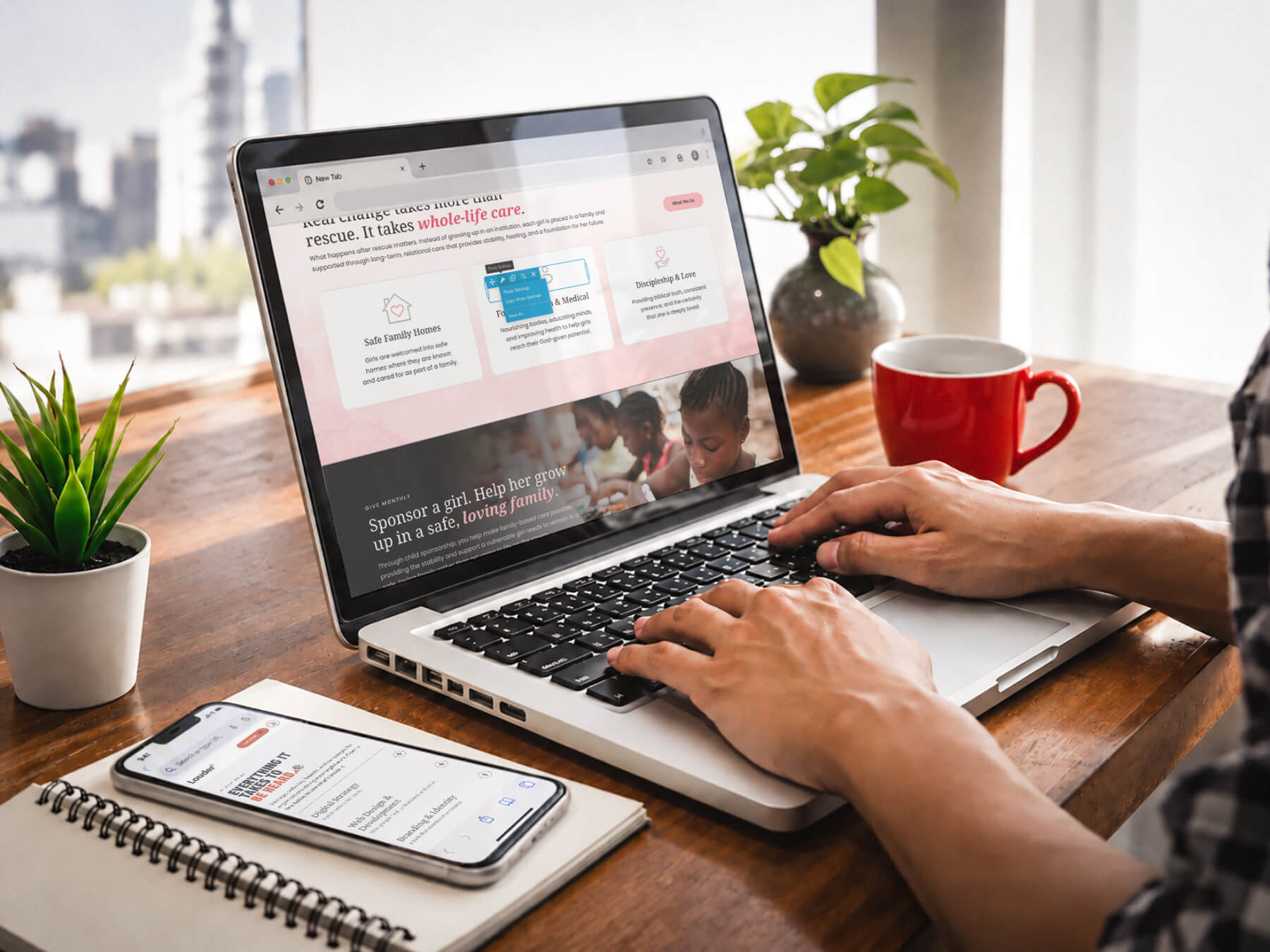Hands on a laptop, working on a nonprofit website, with a phone showing the same site beside it